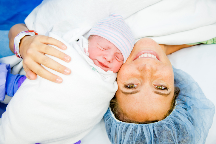 First look after Cesarean Section C-Section Birth. Mother smiling at view with her Newborn following surgery.