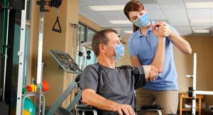 Physical Therapist And Patient In Wheelchair Wearing Protective Masks