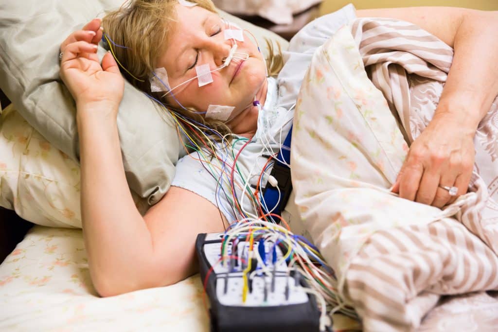 Woman sleeping in a bed in the hospital with equipment attached during a sleep study