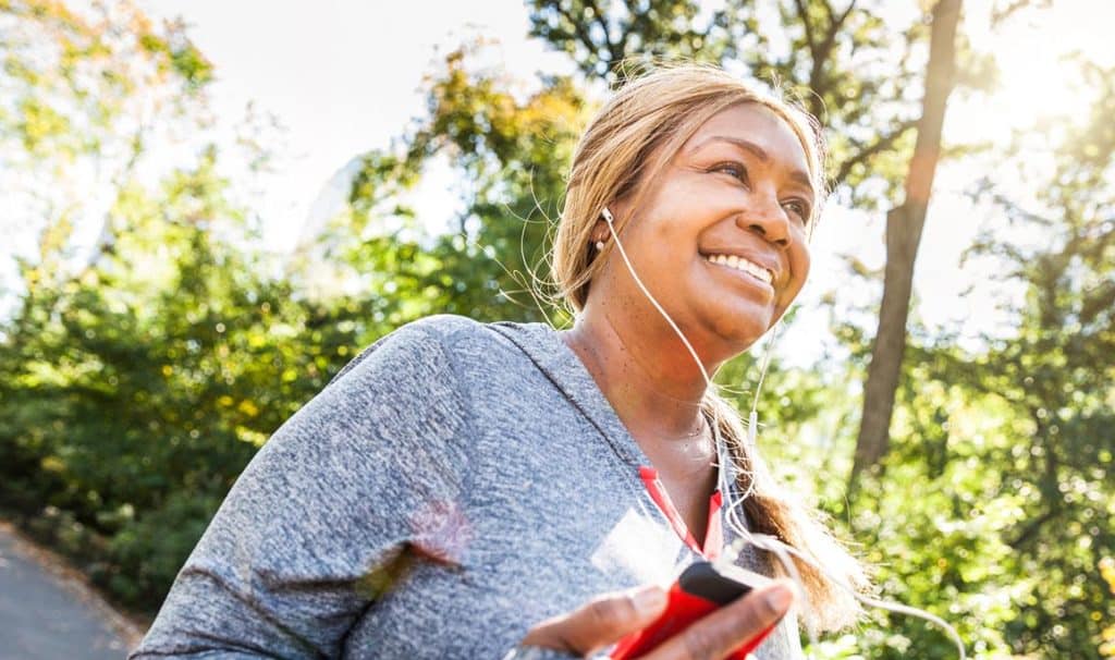 Woman wearing headphones and smiling as she runs on a trail