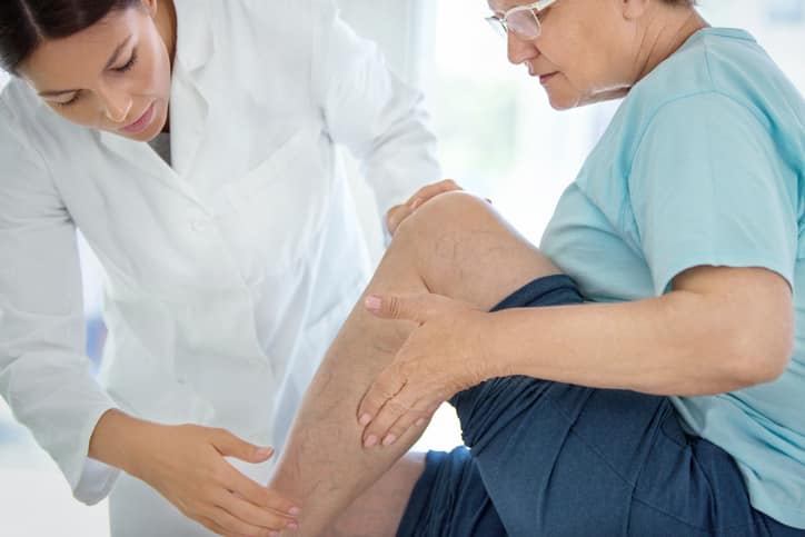 Female doctor massaging legs and calves of a senior female patient with visible varicose veins