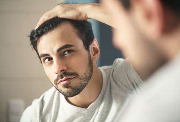 Worried man inspecting his hairline in the mirror