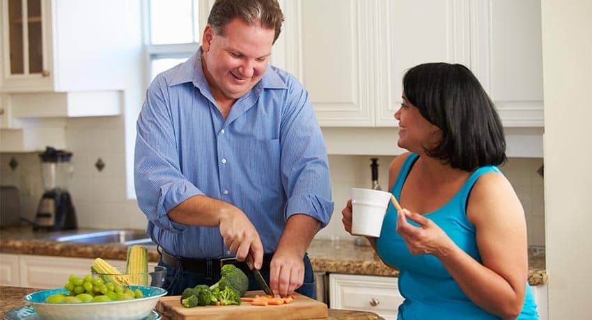 Man slicing vegetables in the kitchen while talking to a woman