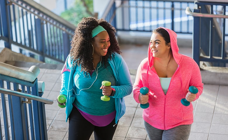 Two women smiling while walking with small weights