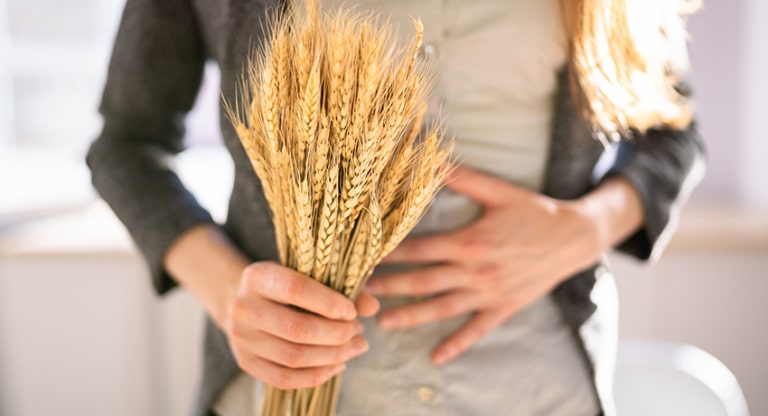 A women holds up wheat grain in one hand and her stomach in another