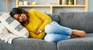 Woman lies on couch with hands over stomach