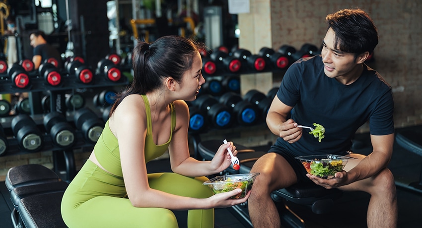 Two young adults eat salad at the gym.