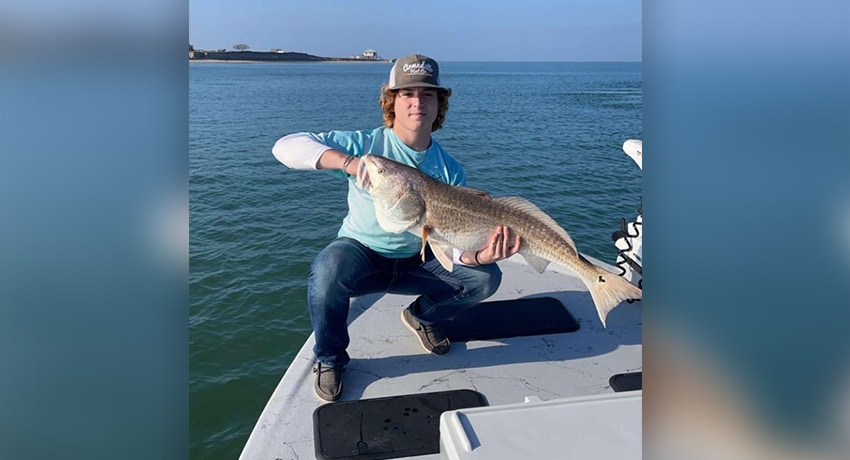 Teen holding a large fish in with both hands on a fishing boat.