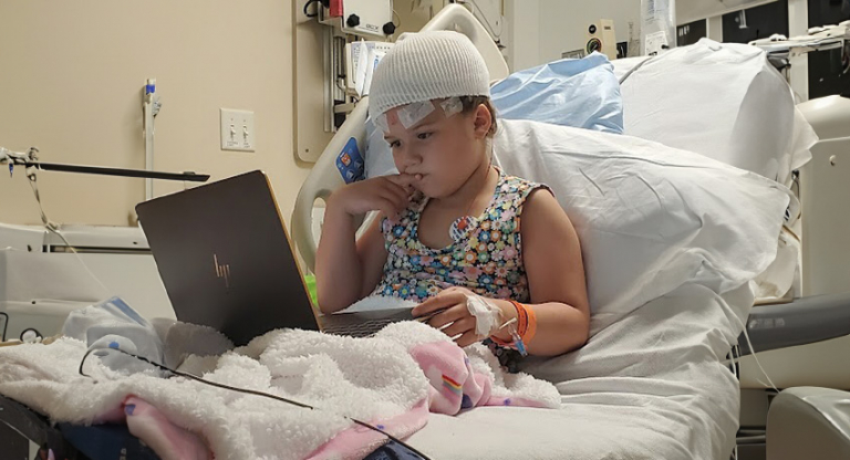 Young girl in hospital bed looking at laptop