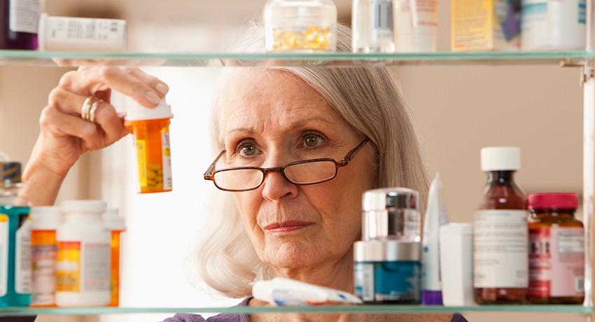 Senior woman looking at prescriptions in medicine cabinet