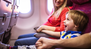 Happy little boy smiling while holding hands with his parents during their travel by airplane.