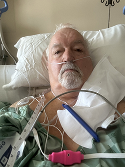 David Fish lying on a hospital bed with tubes and wires draped across his chest after carotid artery procedure