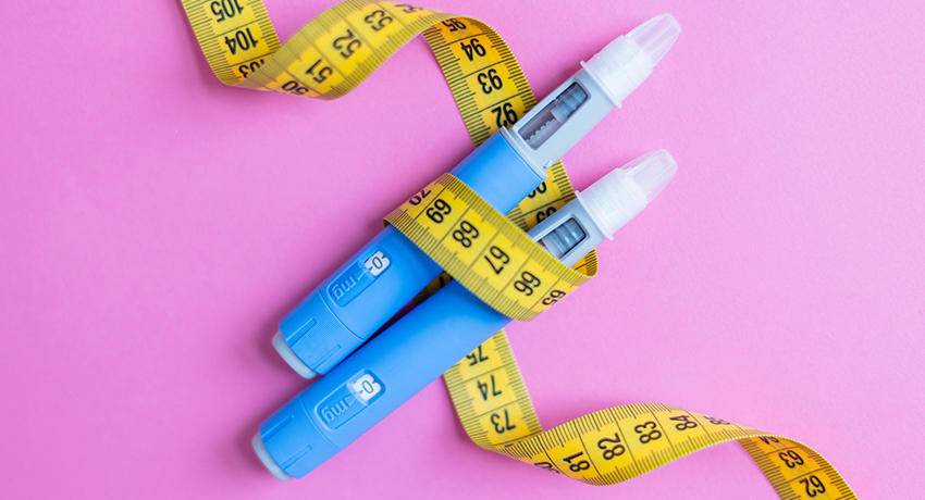 Two blue insulin pens wrapped with a yellow measuring tape on a pink background