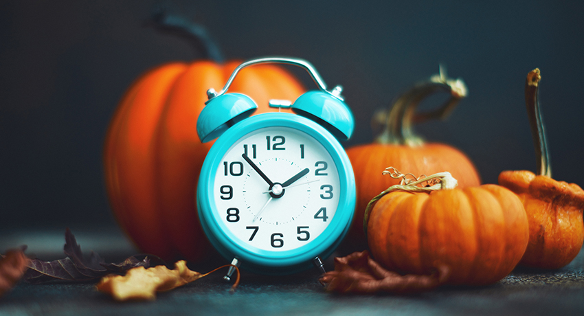 blue clock sitting beside fall pumpkins