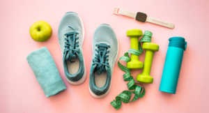 Healthy lifestyle and fitness concept. Sneakers, dumbbells, towel, green apple and fitness bracelet. Flat lay on pink.