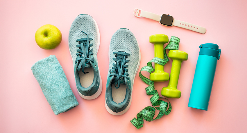 Healthy lifestyle and fitness concept. Sneakers, dumbbells, towel, green apple and fitness bracelet. Flat lay on pink.