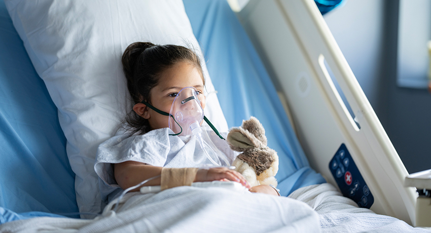 little girl lays back in a hospital bed with an oxygen mask on as she battles RSV