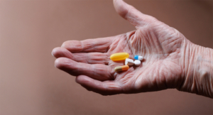 Elderly woman's hand holding various pills and capsules