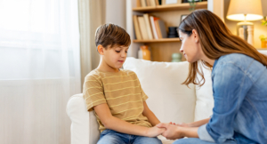 Caring mother holding hands and comforting her sad pensive son while talking to him at home