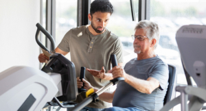 Senior man using exercise equipment with a physical therapist.