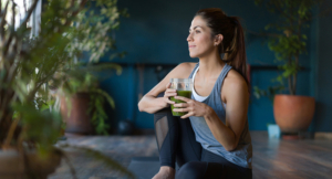 Fit woman drinking smoothie on the floor with exercise mats