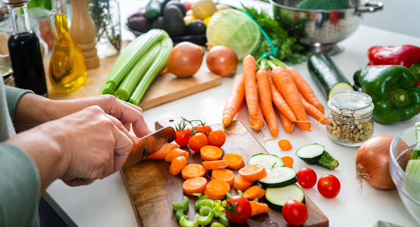 Close up of woman's hands slicing fresh organic carrots on kitchen counter