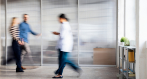 Blurred medical staff and visitors walk through a bright clinic corridor, conveying motion and busy healthcare.