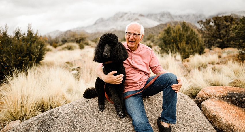 Byron McCormick is sitting with his dog in an outdoor, mountainous setting.